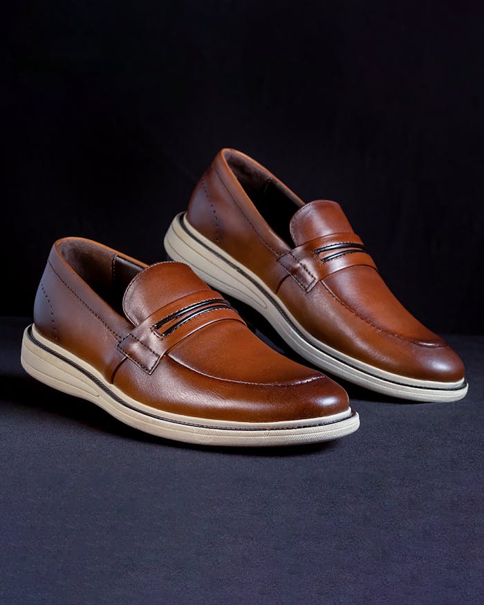 Stylish brown leather loafers displayed against a black backdrop for fashion-focused photography.