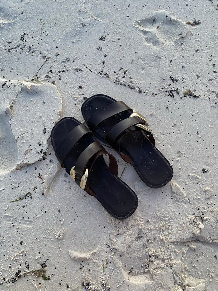 services-01 A pair of black sandals resting on a pristine white sand beach in the Maldives, capturing footprints and serenity.
