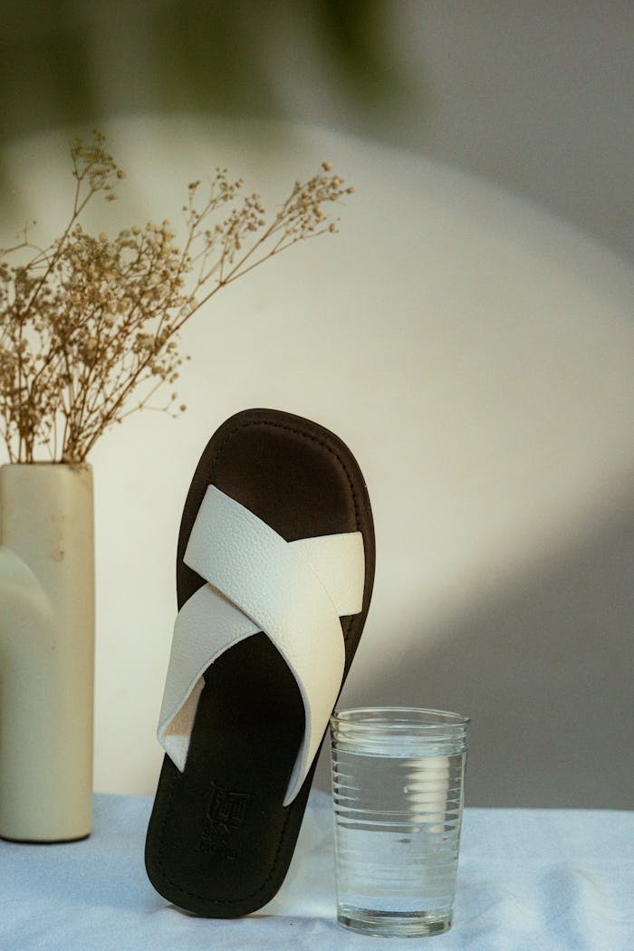 services-03 A stylish sandal with a glass of water and dry flowers in a vase on a table.