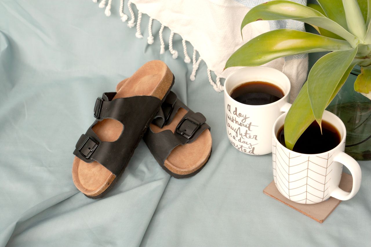 Casual sandals and coffee cups on a cozy setup with a plant, perfect for a relaxed summer morning.