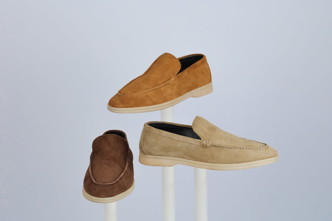 services-02 Three suede loafers showcased on stands, highlighting style and elegance.