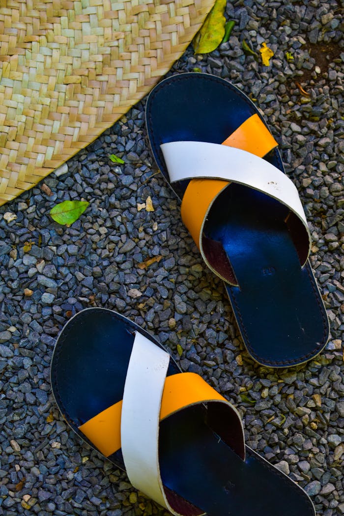 services-img Pair of colorful sandals on a pebbled ground next to a straw hat.