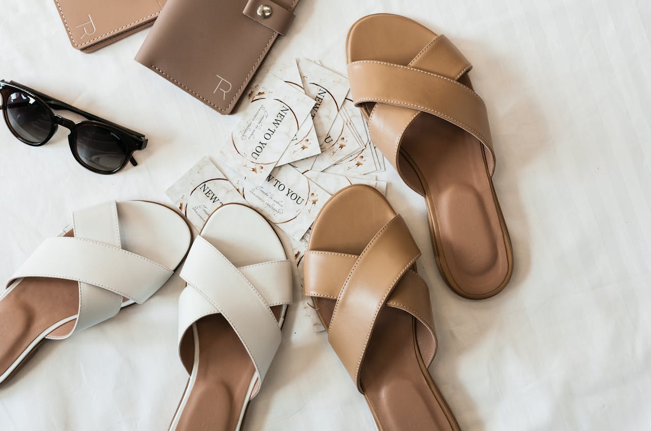 about-img Flat lay of elegant leather sandals, sunglasses, and wallet on a neutral background.